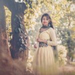 Portrait of a woman in traditional South Asian attire standing outdoors under trees.